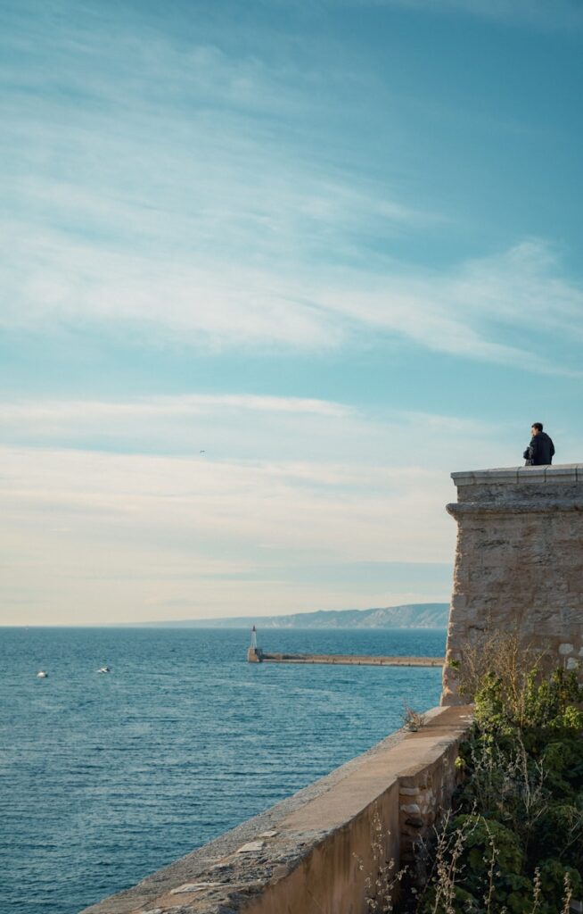 a person sitting on a ledge overlooking the ocean